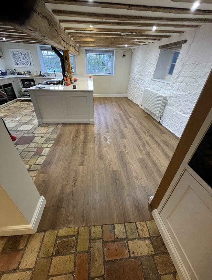 Open-plan Cambridge kitchen with Croft Oak LVT flooring framed by original brick tiles and white shaker cabinetry