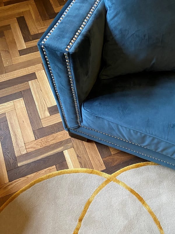 Blue velvet sofa and pale rug on oak basketweave parquet flooring, close-up.