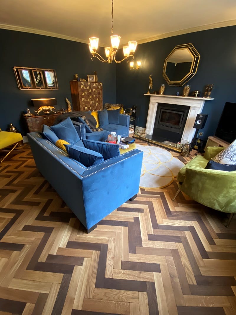Full lounge view with oak basketweave parquet flooring, blue walls, and velvet seating.
