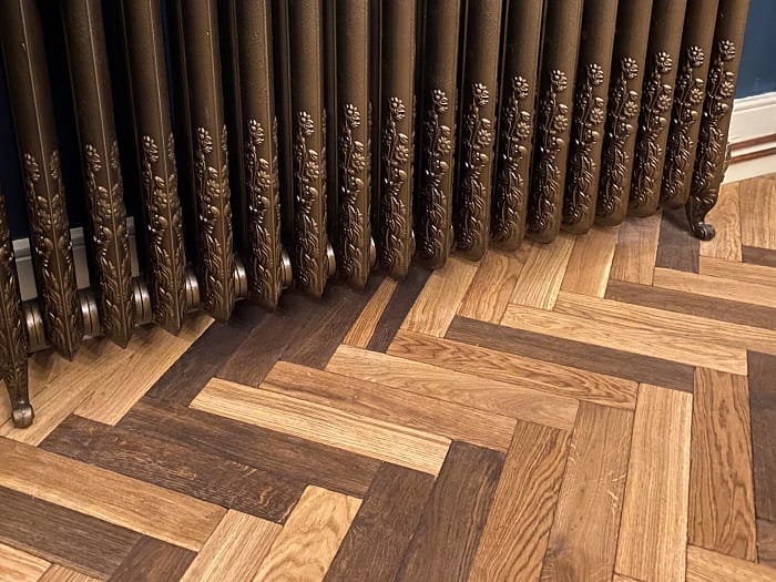 Cast iron radiator beside oak basketweave parquet flooring, close-up detail.