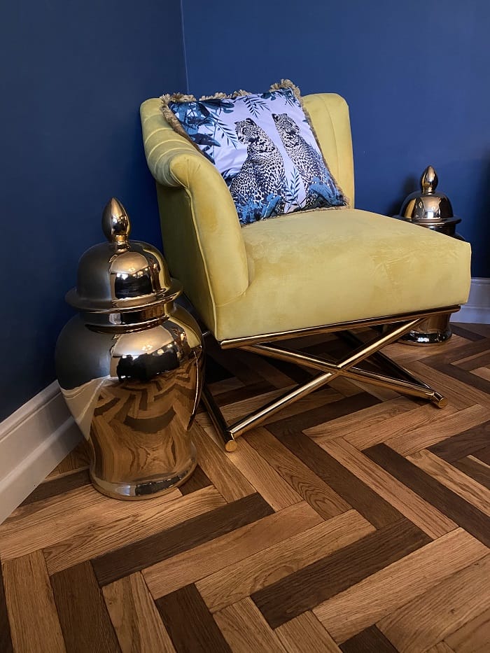 Close-up of yellow velvet chair on oak basketweave parquet flooring with brass base.