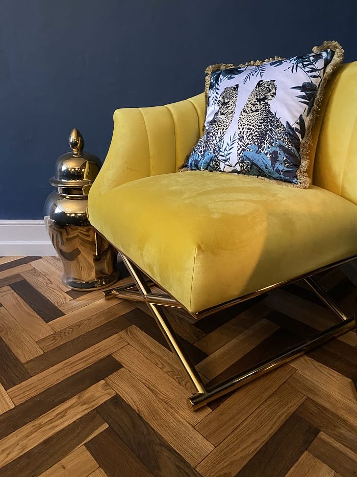 Close-up of yellow velvet chair on oak basketweave parquet flooring with brass base.