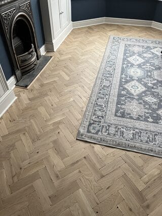 Oak herringbone parquet flooring installed in a Cambridge living room beside a traditional cast iron fireplace.