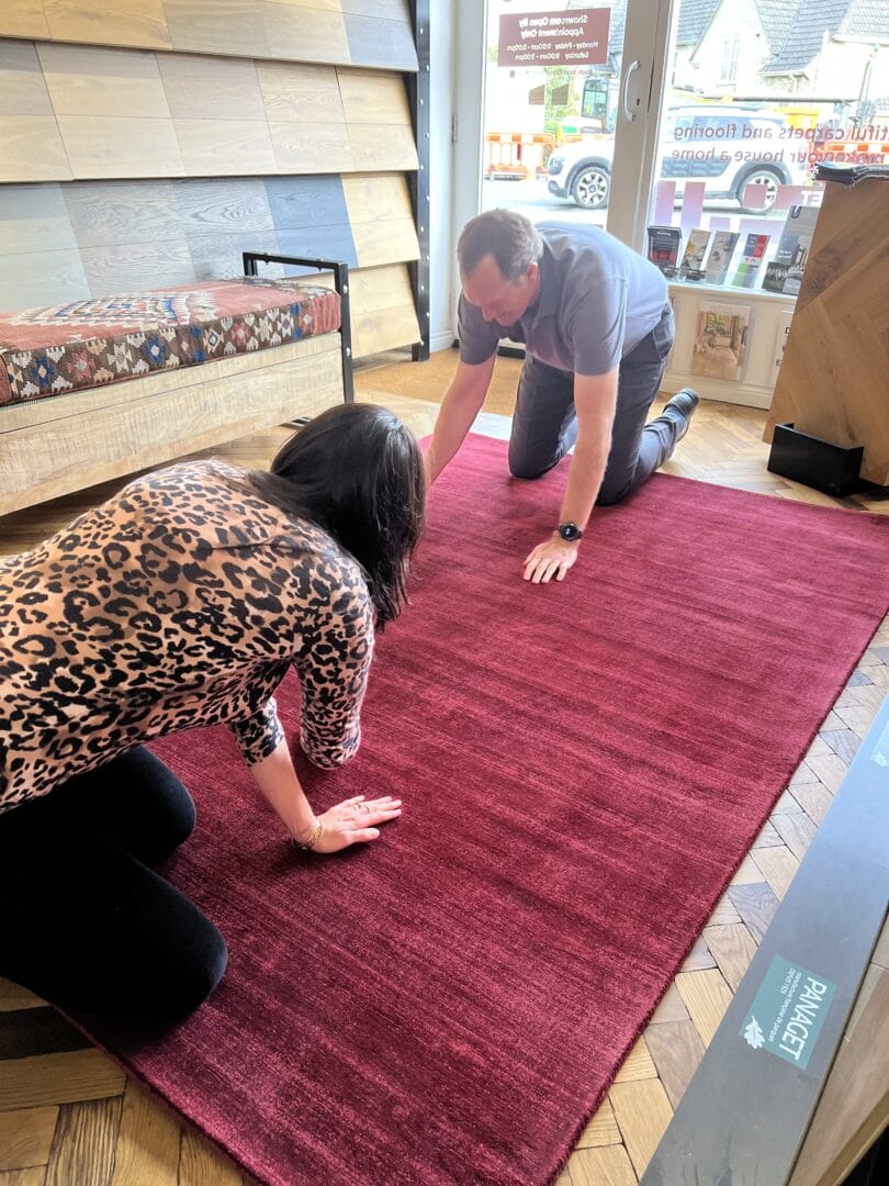 Customers testing a red rug on a wood floor inside the Art of Flooring Cambridge showroom.