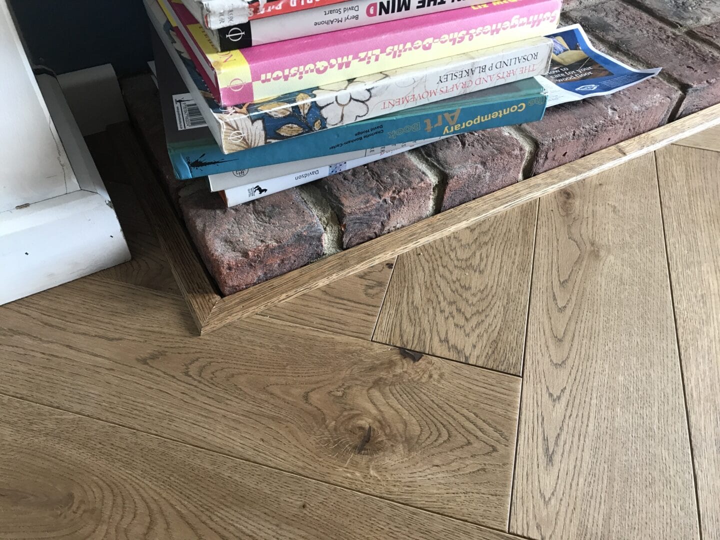 Oak flooring detail around brick hearth with books in Cambridge home