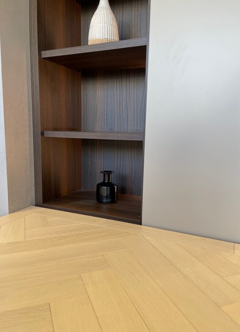 Oak herringbone flooring detail beside dark wood shelving unit in Cambridge home