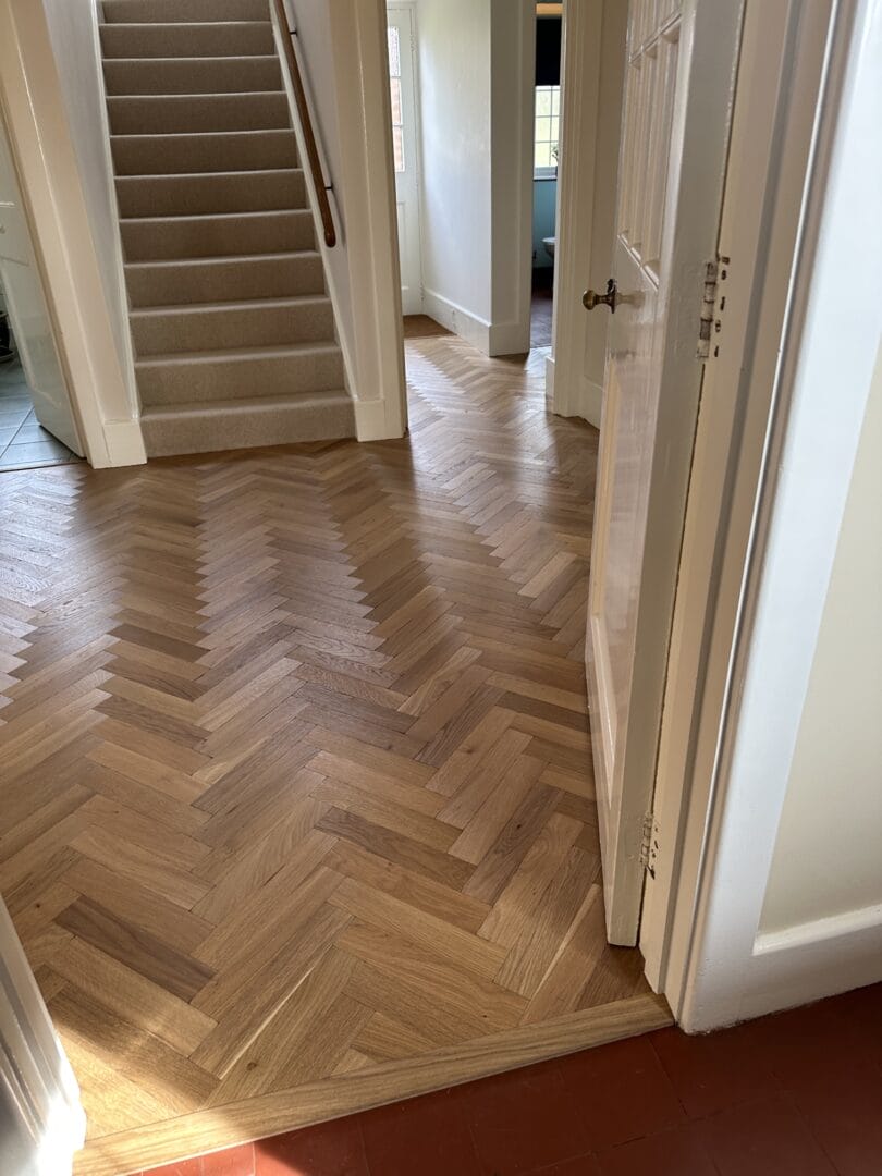 Oak herringbone flooring installed through a Cambridge hallway leading to stairs
