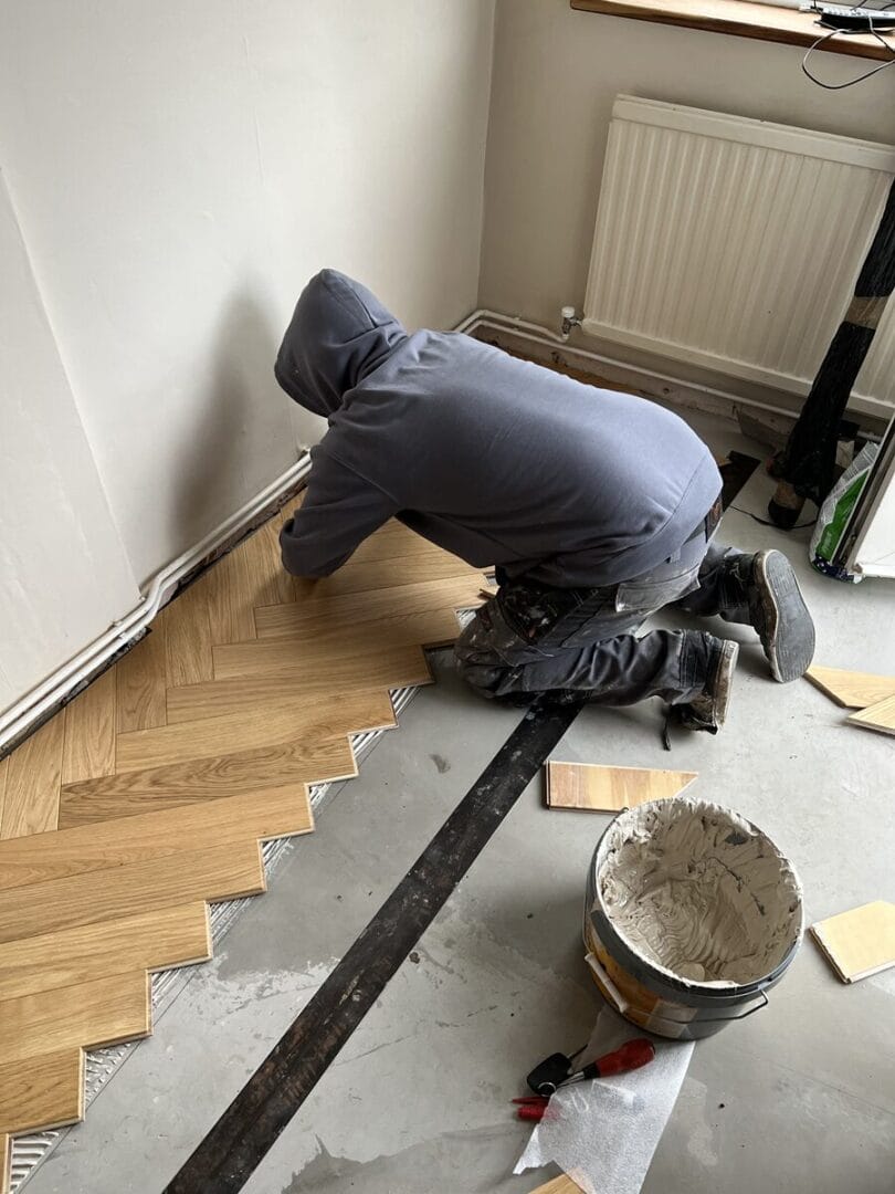 Installer laying engineered oak herringbone flooring during a Cambridge flooring project.