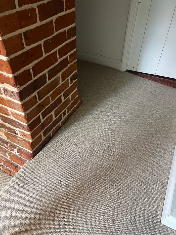 Natural loop carpet installation in a cottage hallway near Cambridge with exposed brick and painted walls.
