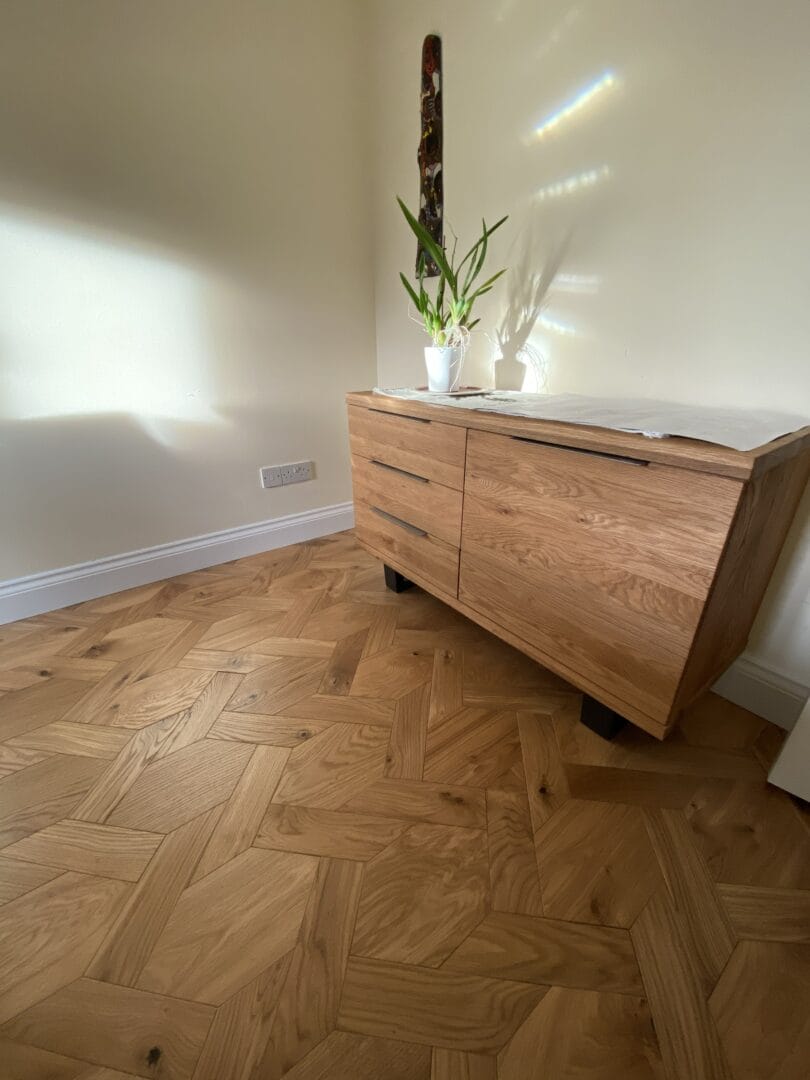 Geometric oak parquet flooring beneath a wooden sideboard in a Cambridge home.