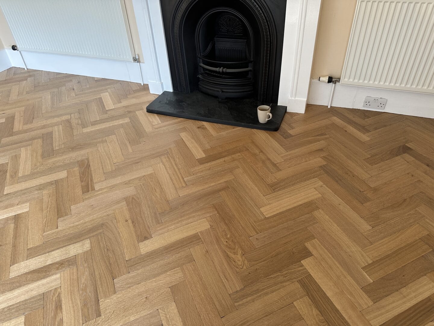 Oak herringbone parquet flooring installed around a traditional fireplace in a Sevenoaks lounge
