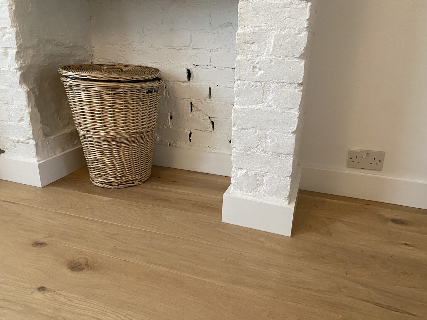Close-up of an oak floor meeting an exposed brick chimney alcove with a wicker basket