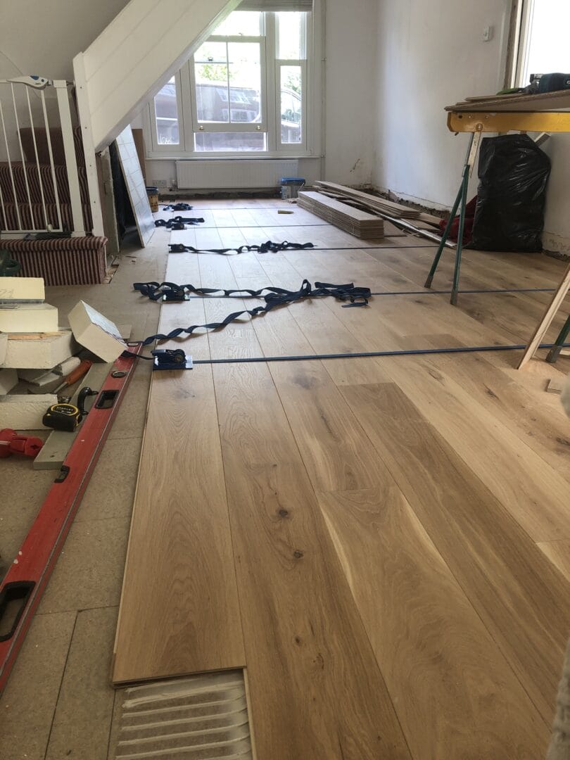 Ash engineered wood floorboards being laid and strapped during installation in a Cambridge home