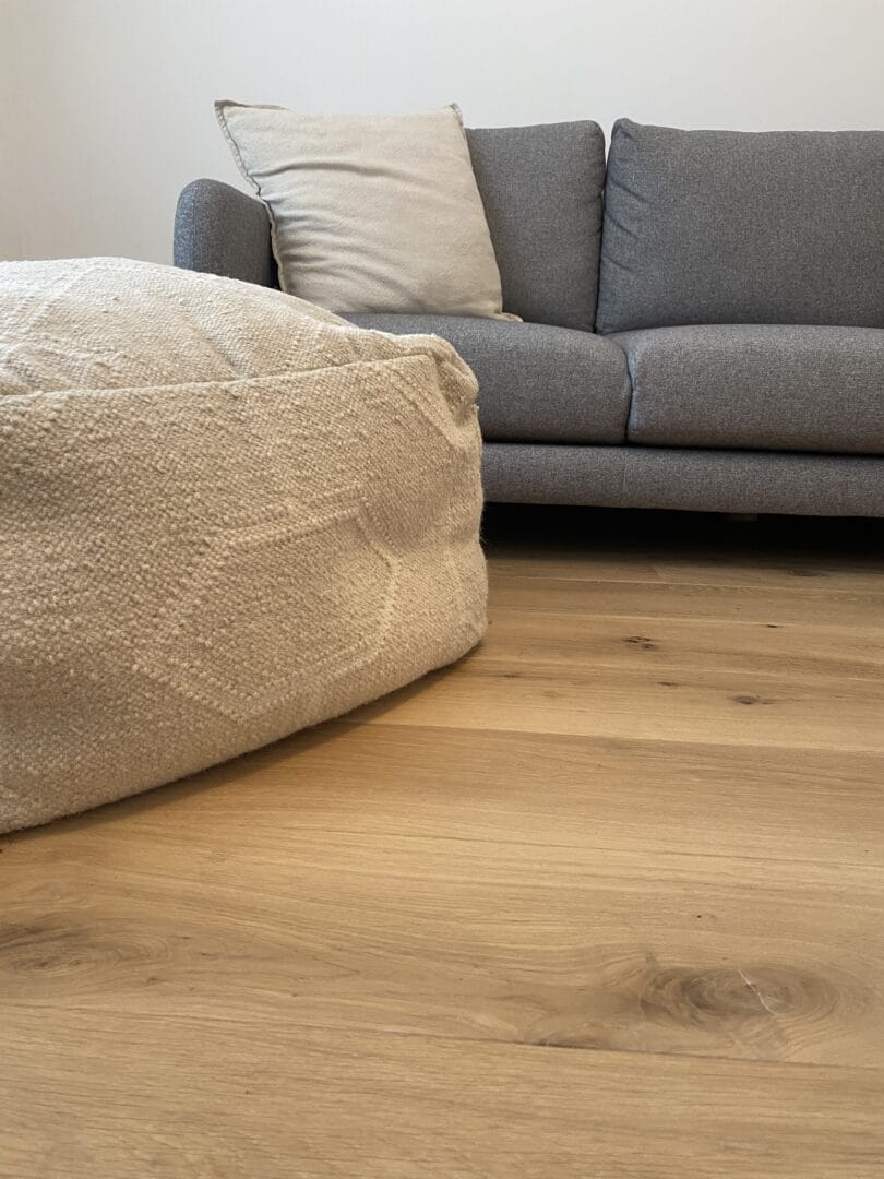 Ash engineered wood floor in a living room with a grey sofa and woven pouf