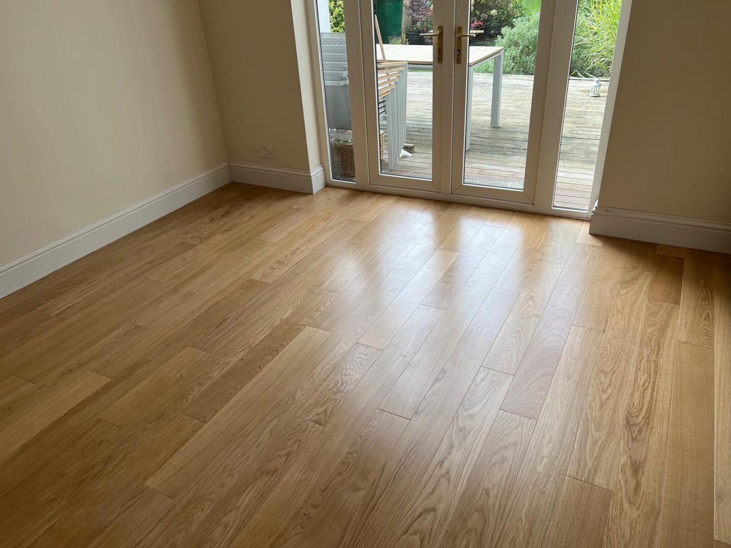Empty room with light oak wood flooring and French doors opening onto a garden decking area