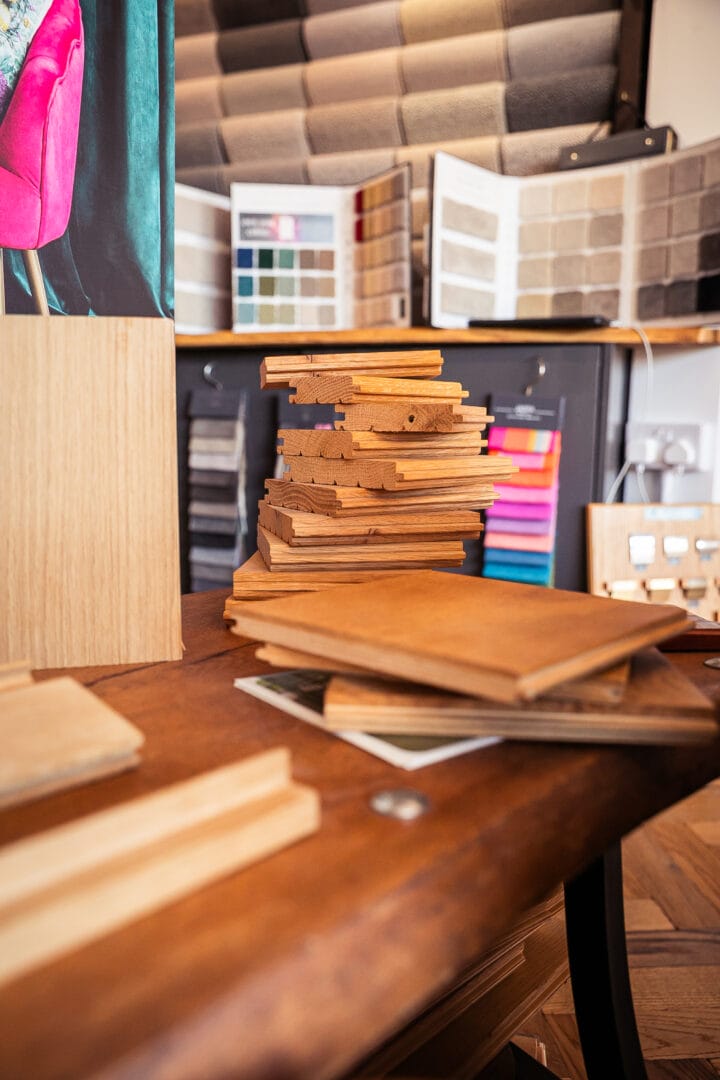 Stack of wood flooring sample mouldings and finish boards on a table in the Art of Flooring showroom, with carpet swatch books in the background