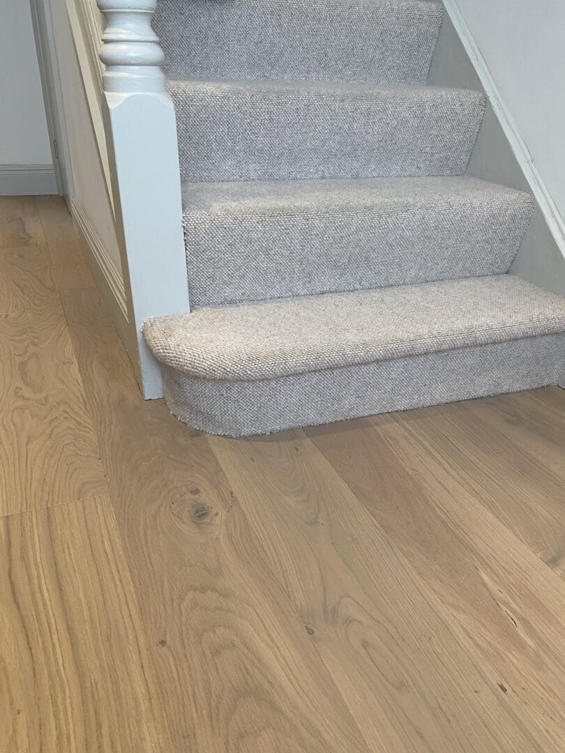 Engineered oak flooring at the foot of a staircase with a grey carpet runner