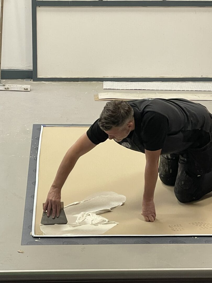 Fitter spreading adhesive with a trowel before laying engineered wood flooring