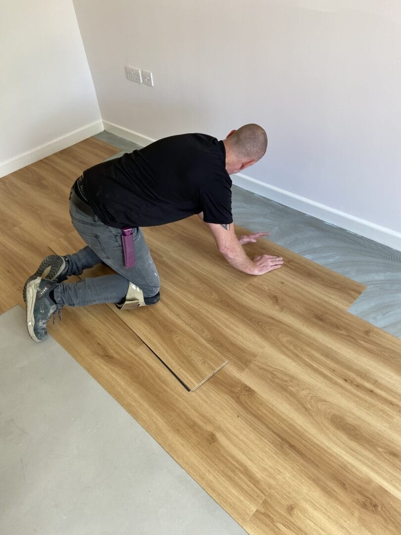 Fitter laying engineered wood flooring boards over adhesive on a Cambridge subfloor
