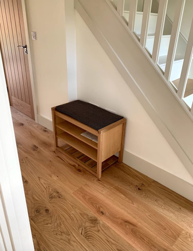 Engineered wood flooring in a hallway leading past an understairs storage bench