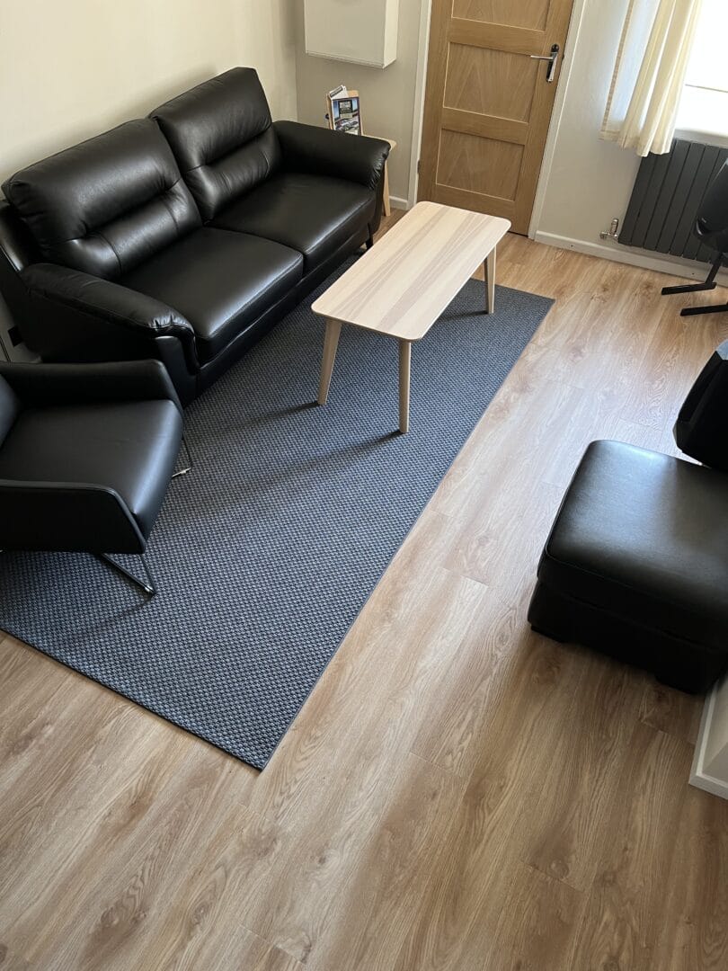 Engineered wood flooring in a lounge with black leather sofas and a runner rug