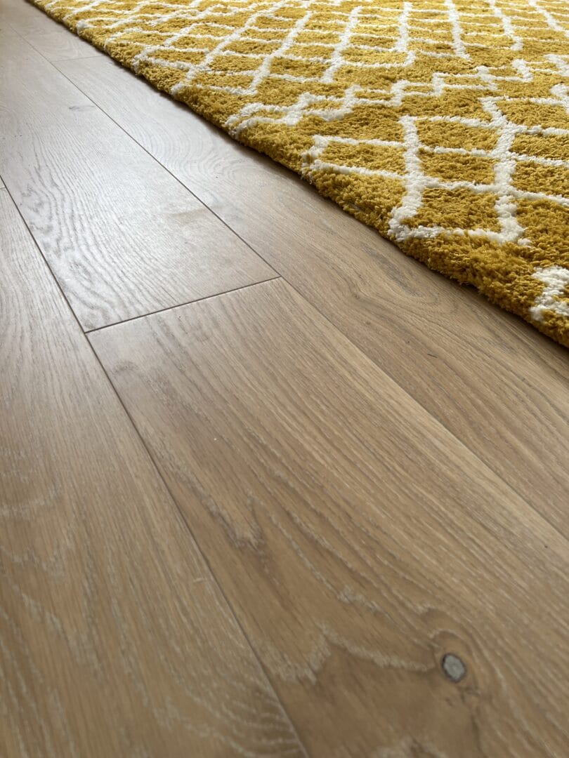 Close-up of engineered wood flooring grain next to a mustard patterned rug