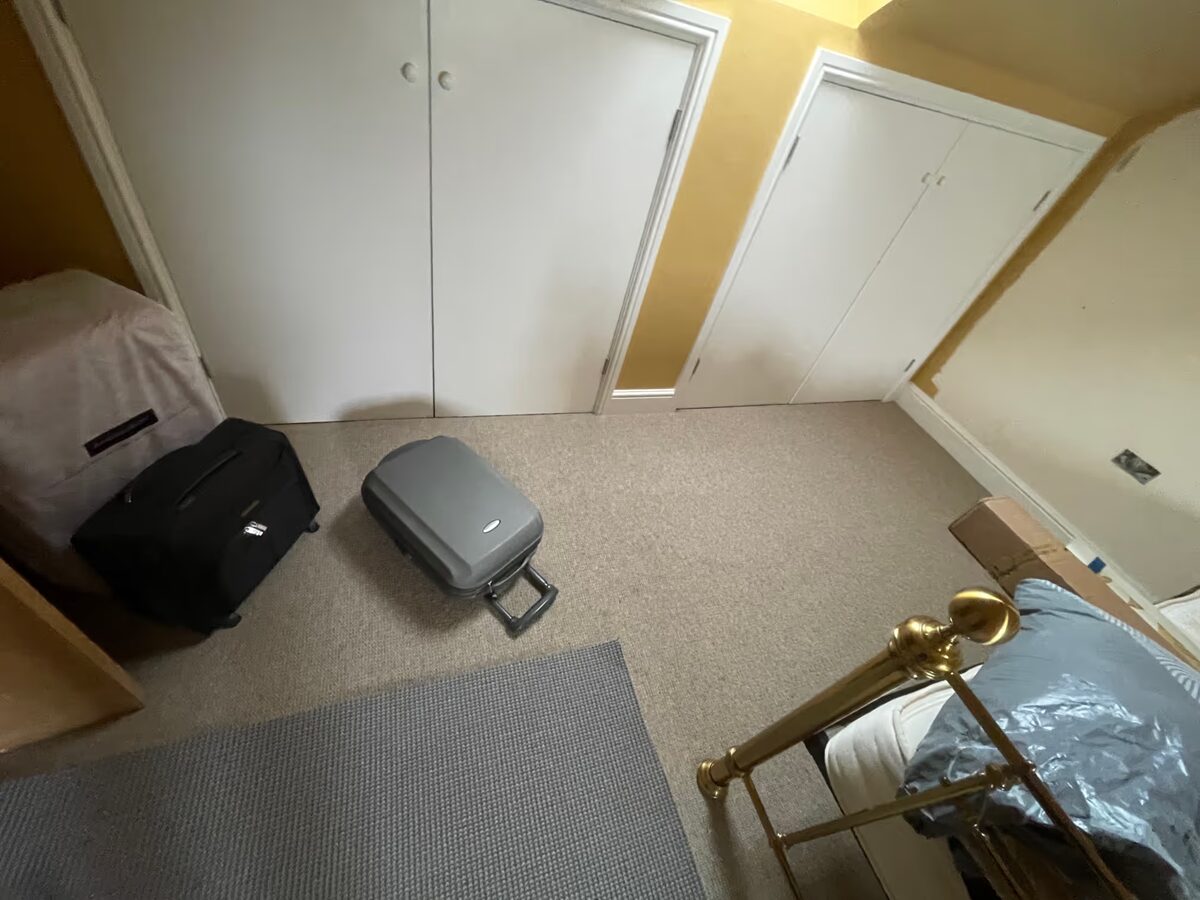 A dressing room with cream carpet, white built-in wardrobes and two suitcases waiting to be unpacked.