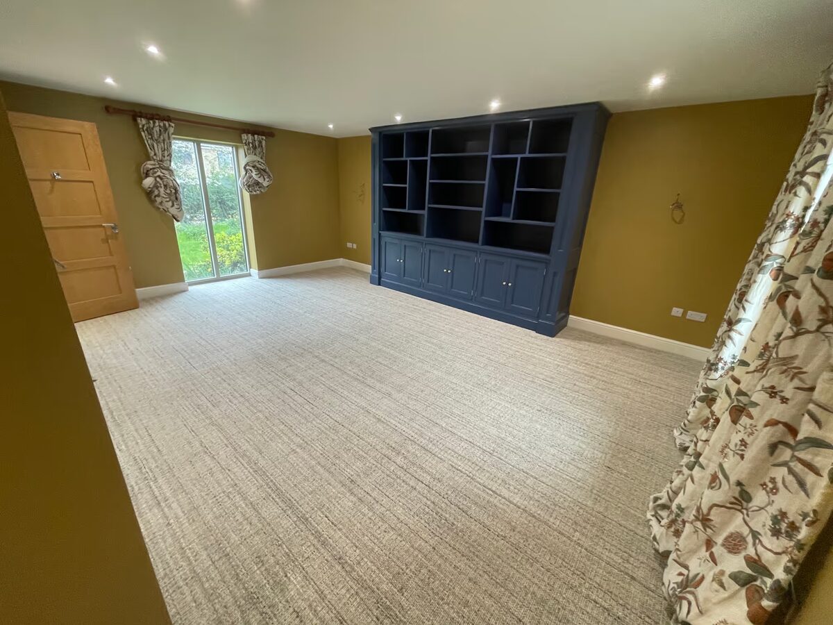 The snug's patio doors overlooking the garden, with the new beige carpet and built-in navy bookcase visible.
