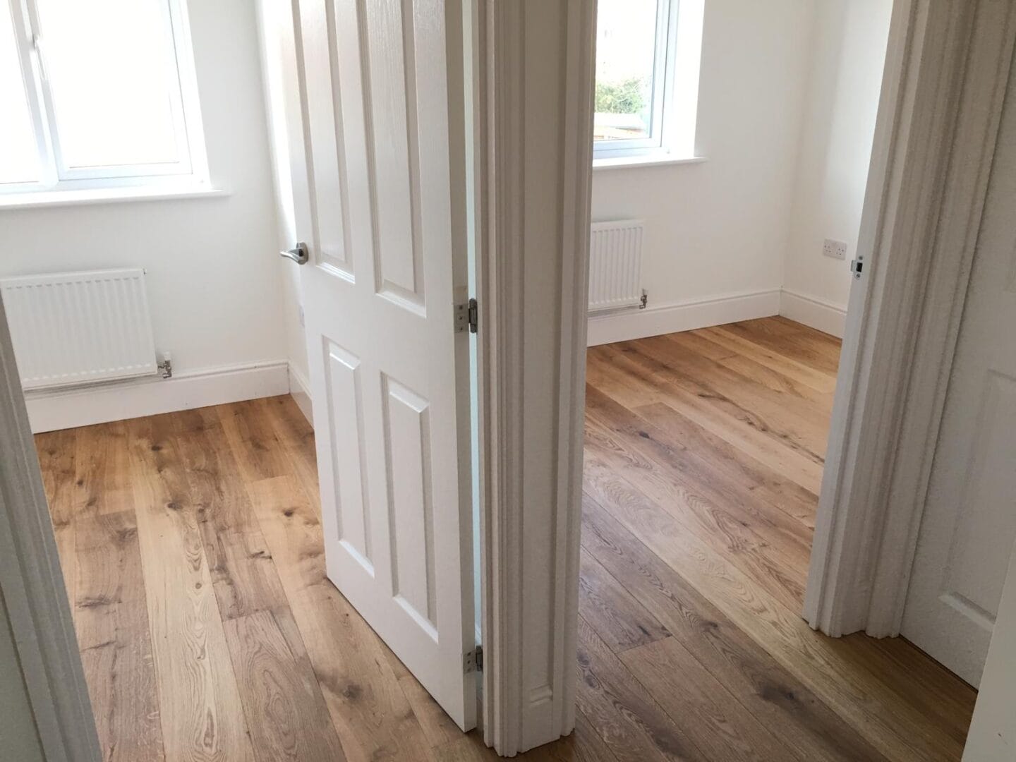 Wide-plank engineered oak flooring running through an open hallway between two bright bedrooms