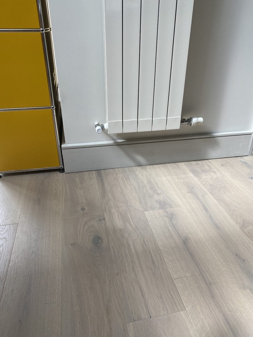 Close-up of pale, whitewashed engineered oak flooring next to a radiator and yellow storage unit
