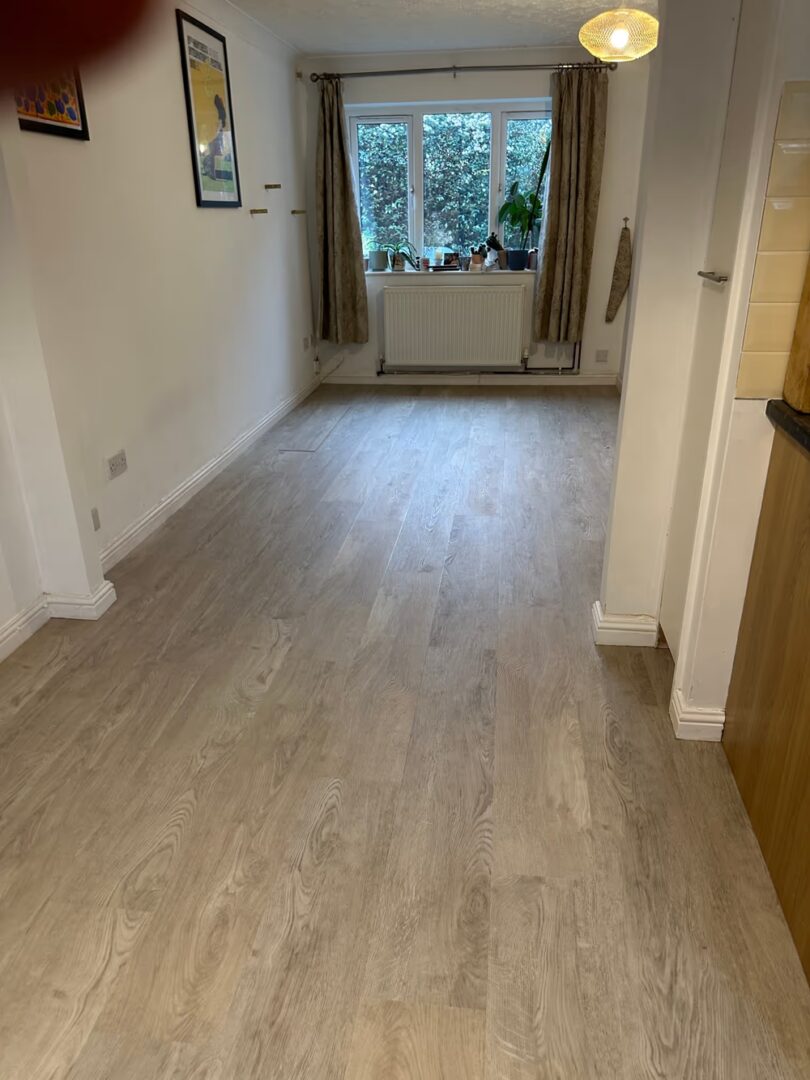 White Oak flooring running down a long room towards a window, with plants on the sill and a radiator below
