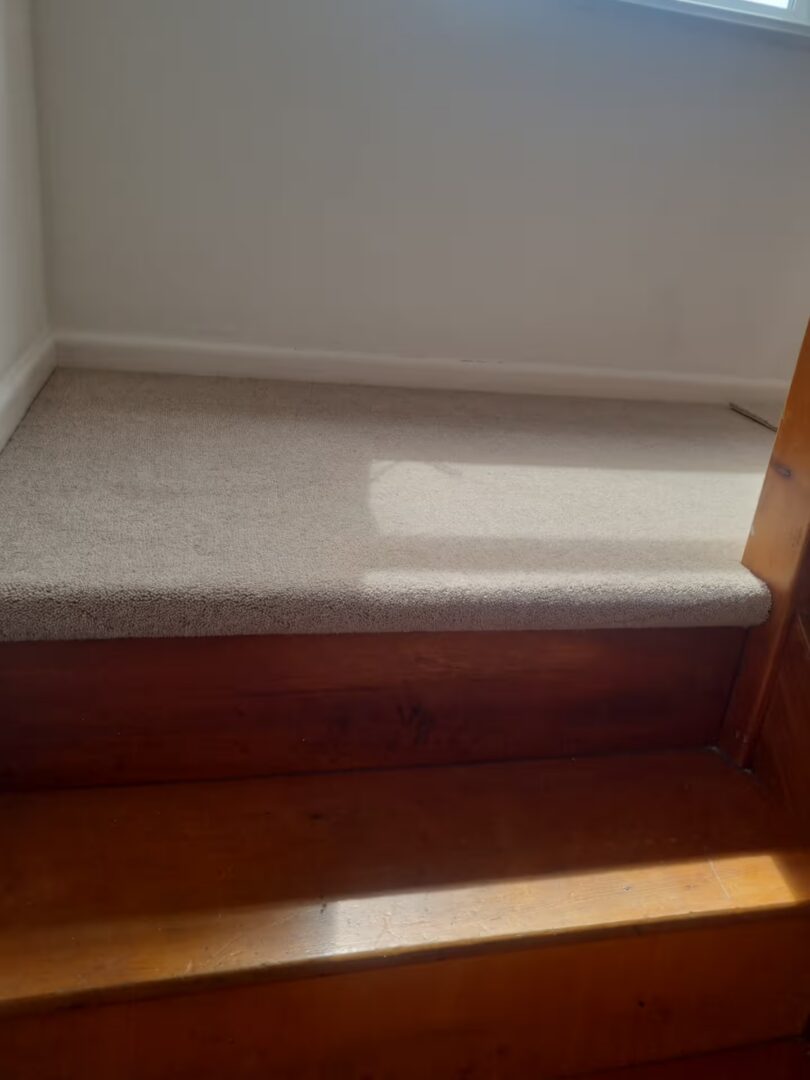 Half landing fitted with beige carpet, with the original wooden stair treads left exposed below.