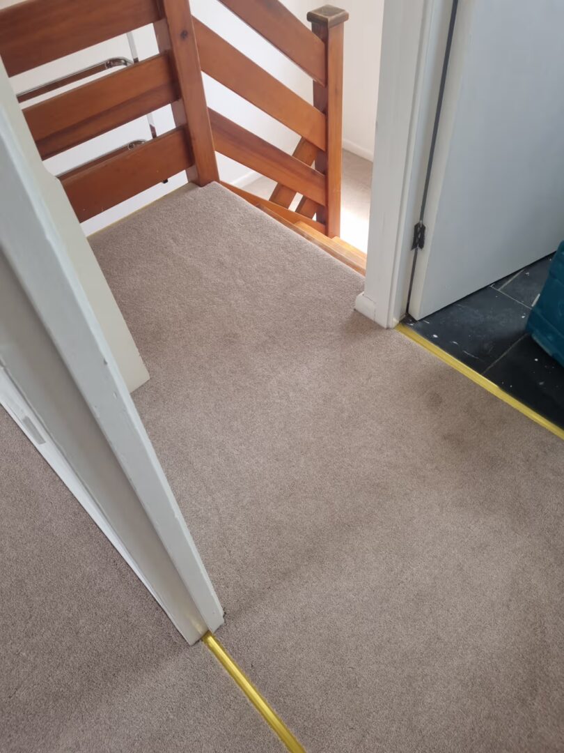 Landing fitted with light beige carpet, with a wooden staircase banister and brass threshold strips at the doorways.