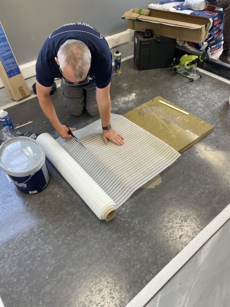Trainer cutting a length of reinforcement mesh from a roll beside the repaired test board.