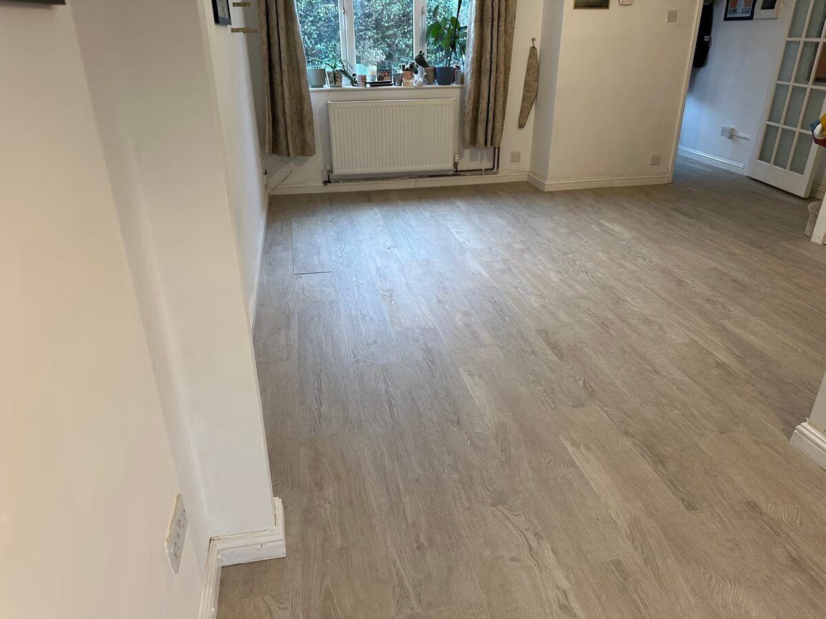 Open-plan living space with White Oak flooring running towards a window and on through a doorway into the hall