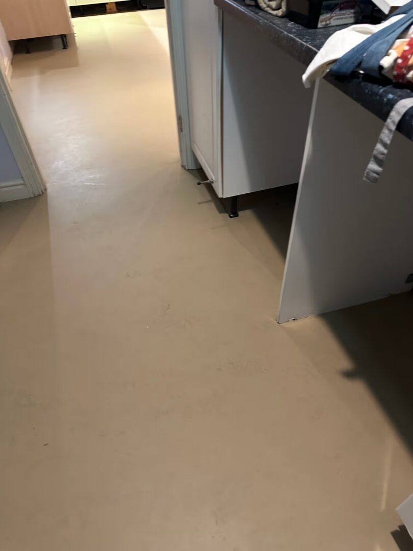 Levelled subfloor next to white base units and a worktop, with the kitchen visible through the doorway