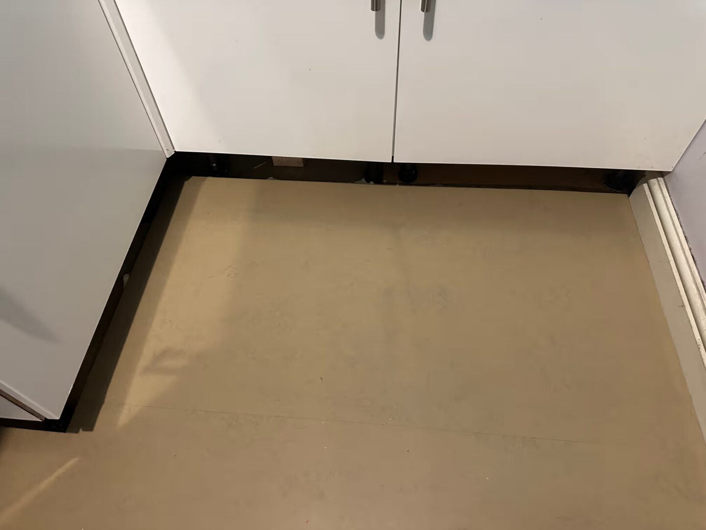 Levelled floor in front of white kitchen units with the plinths removed, exposing the cabinet legs