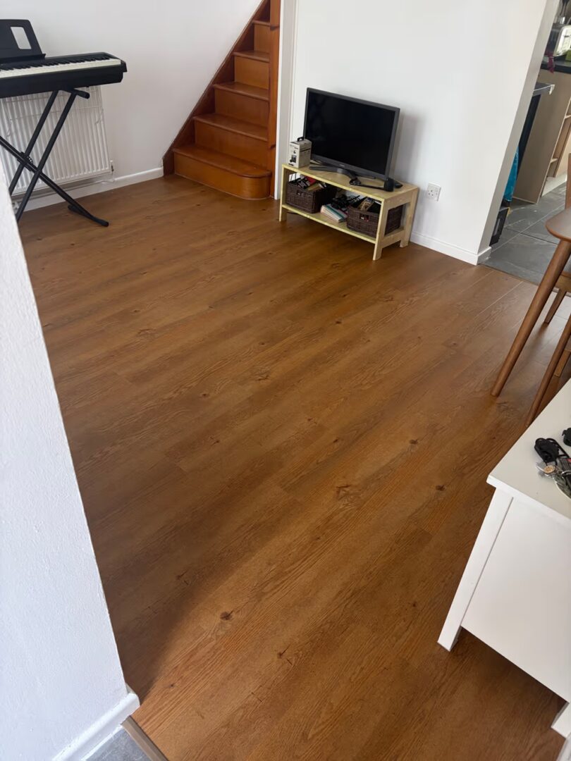 Living room with oak effect vinyl flooring leading to an original wooden staircase in a closely matching tone.